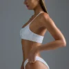 Oh Polly Moda kąpielowa: Top bikini bandeau z jednym ramiączkiem z ozdobami z serii HOTFIX w kolorze białym Oh Polly Moda kąpielowa: Top bikini bandeau z jednym ramiączkiem z ozdobami z serii HOTFIX w kolorze białym